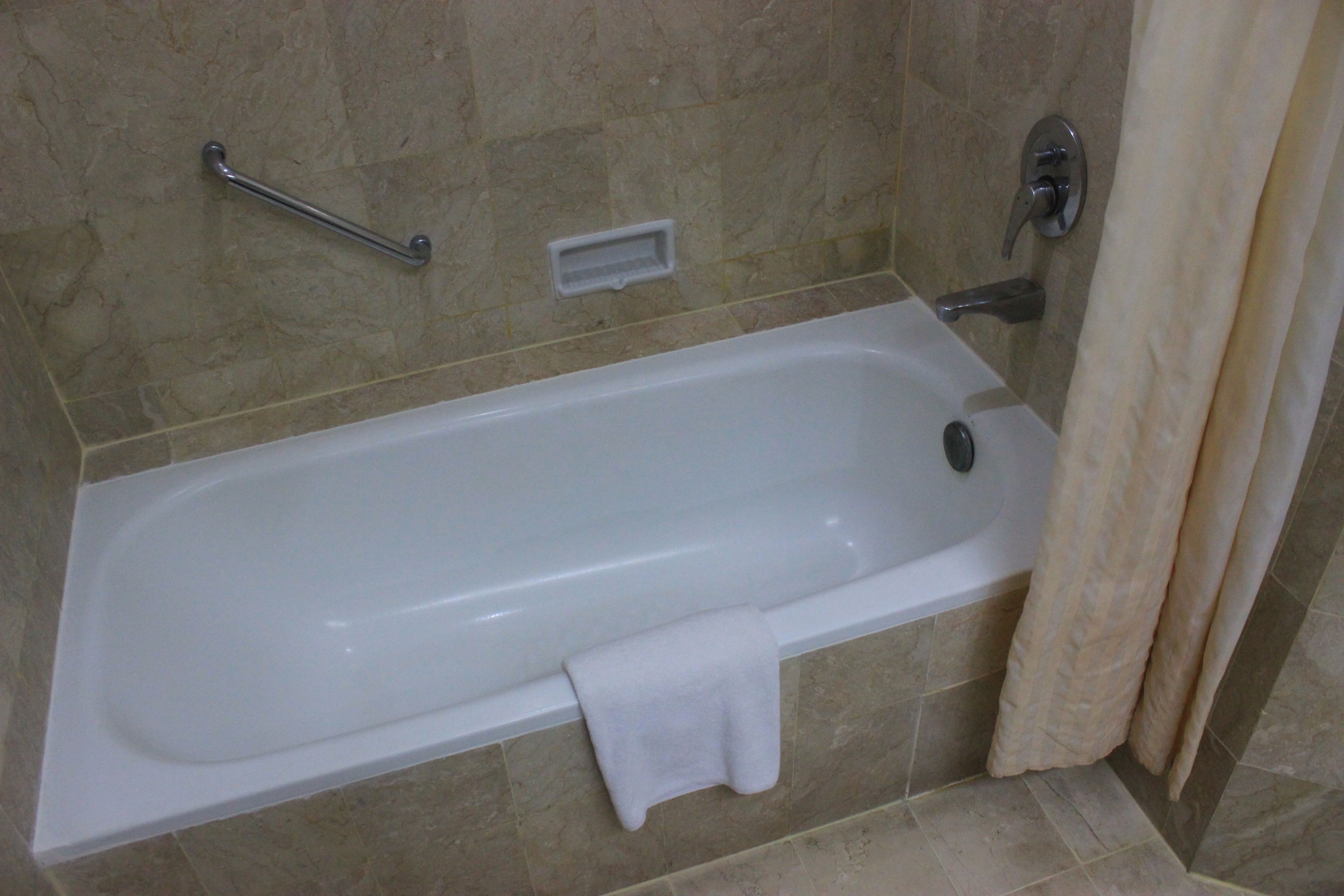 A standard bathtub with a grab bar, a towel, and a shower curtain in a bathroom with beige tiles.