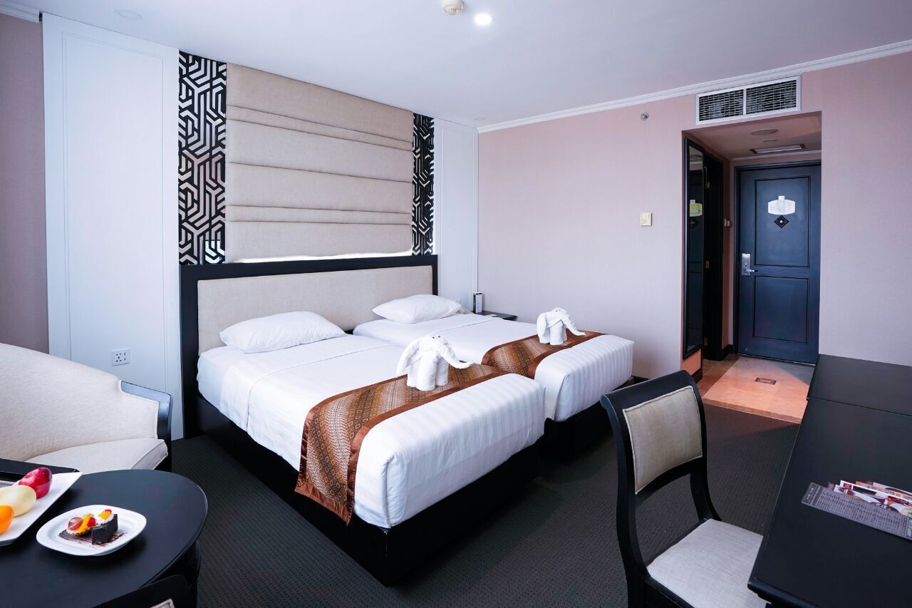 A hotel room with a bed, two bedside tables, a chair, a small table with a plate of food, and a door.