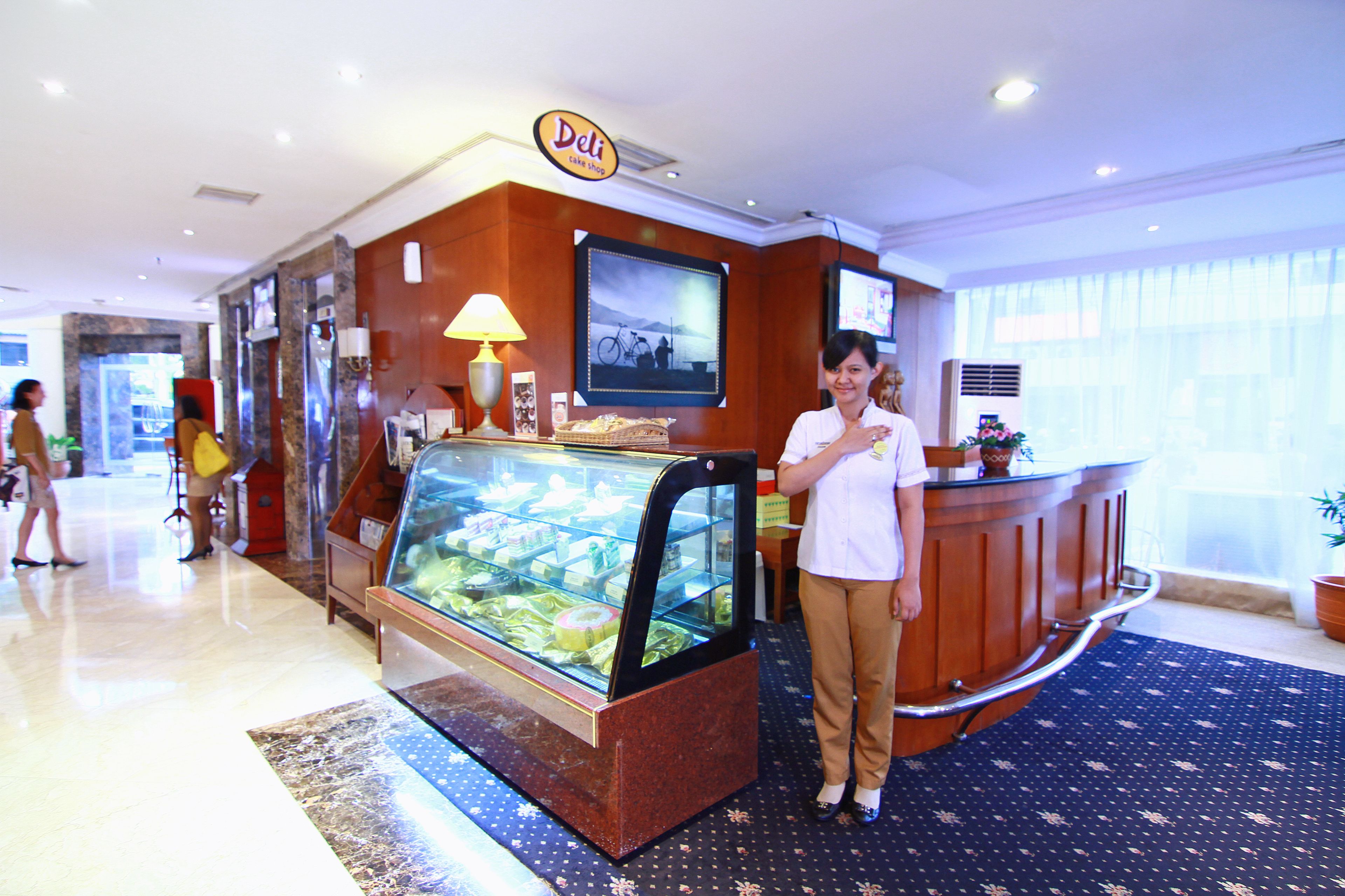 Ein Hotel-Empfangsbereich mit einer Feinkosttheke, einer Glastheke mit Lebensmitteln und einer Rezeption.