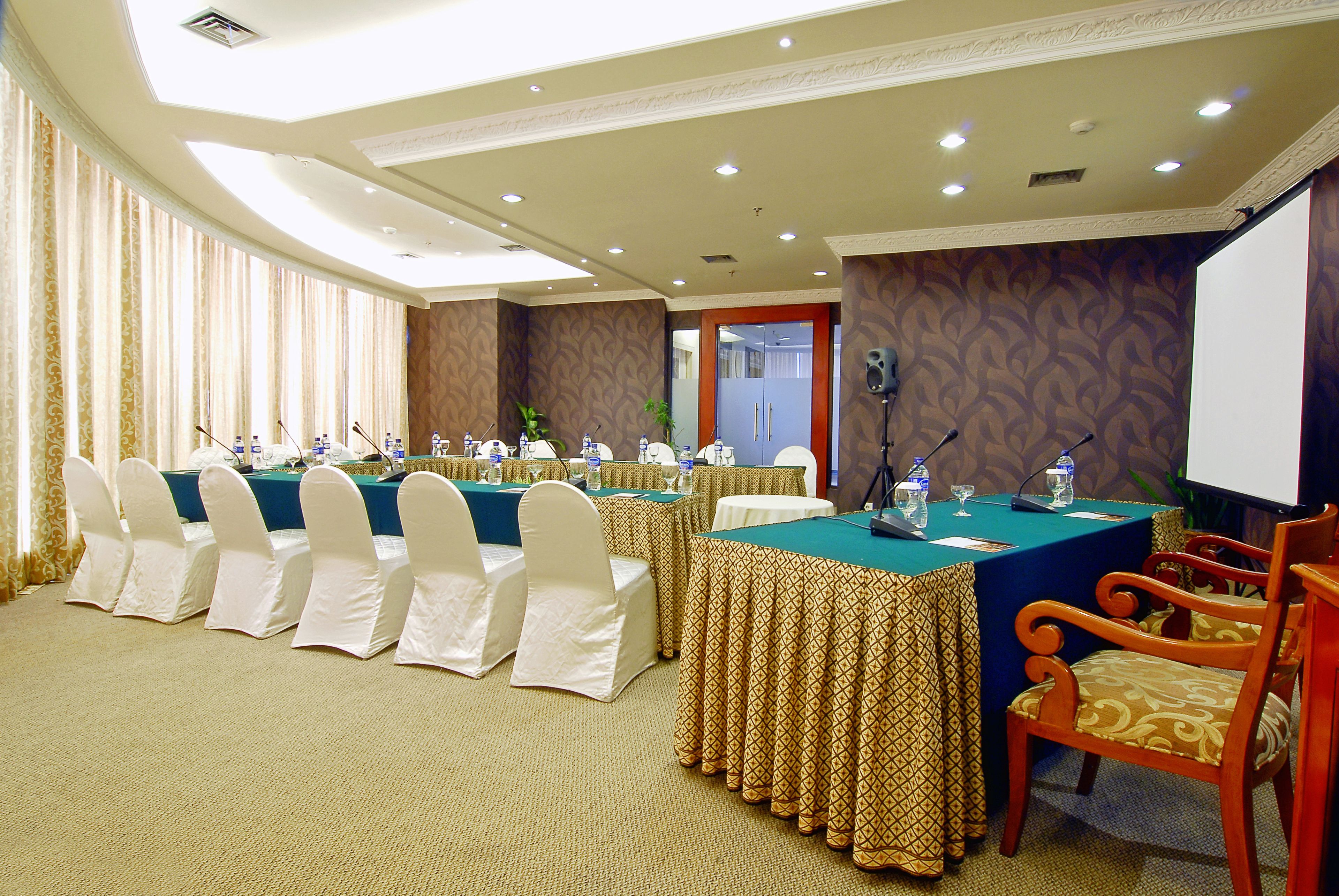 A conference room with tables, chairs, microphones, and a projector screen.
