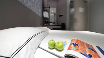 A hotel room with a neatly made bed, two green apples on the bed, and a magazine open on the bed.