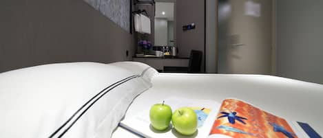 Una habitación de hotel con una cama bien hecha, dos manzanas verdes sobre la cama y una revista abierta.