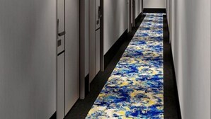 Un pasillo largo y estrecho con puertas a un lado y una alfombra estampada en el suelo.