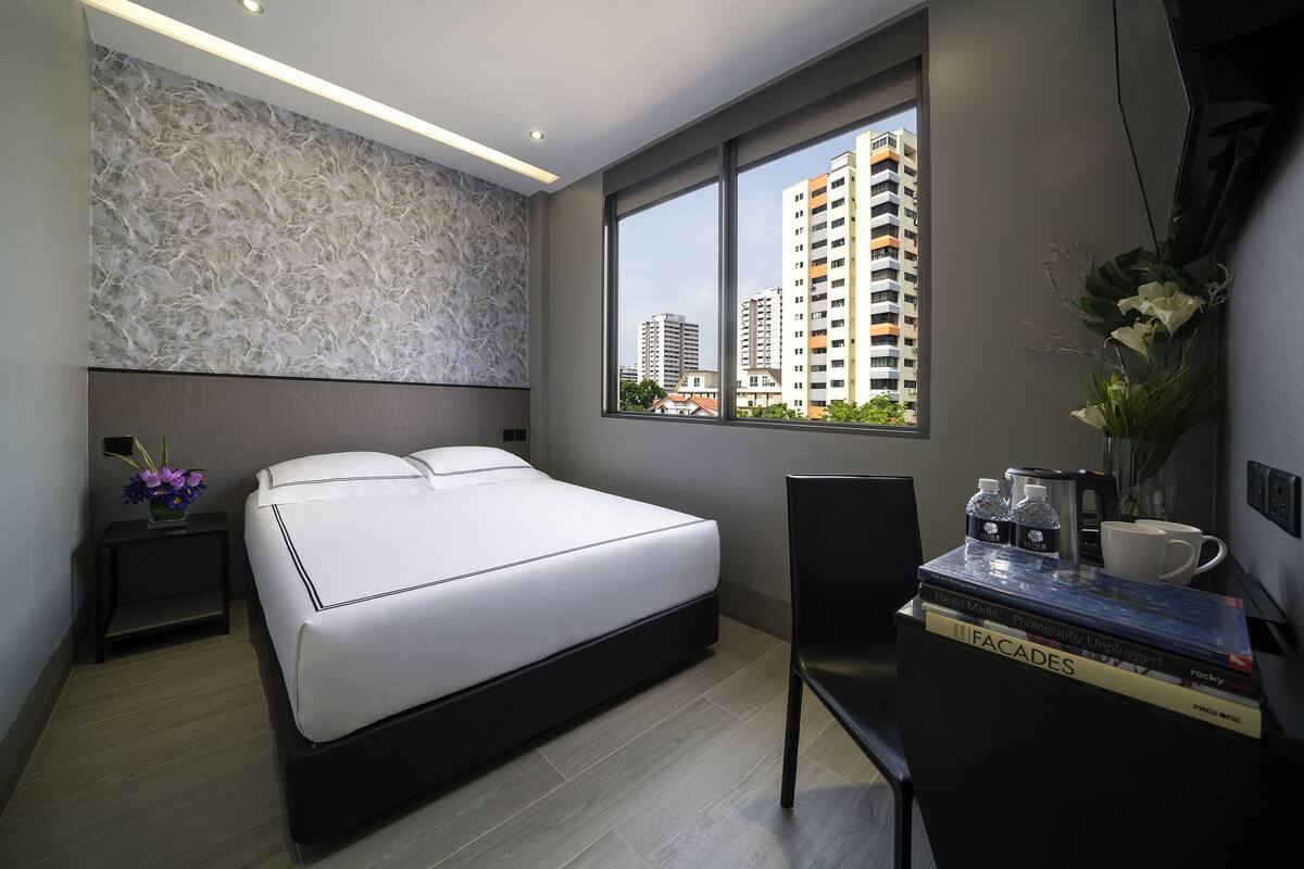 Een moderne hotelkamer met een groot bed, een bureau met boeken, een koffiezetapparaat en uitzicht op hoge gebouwen.