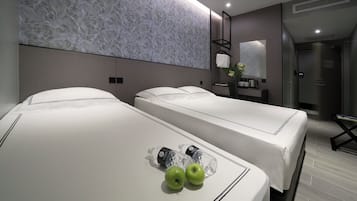 Ein Hotelzimmer mit zwei Betten, einer Marmorwand, einem Spiegel, einem kleinen Tisch mit einer Vase und einer Tür.