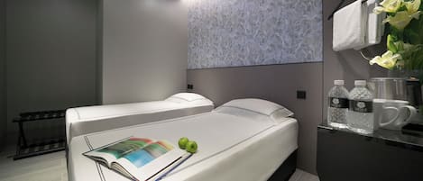 A modern hotel room with a large bed, a bedside table with a magazine and apples, a mirror, and a wall with a textured pattern.
