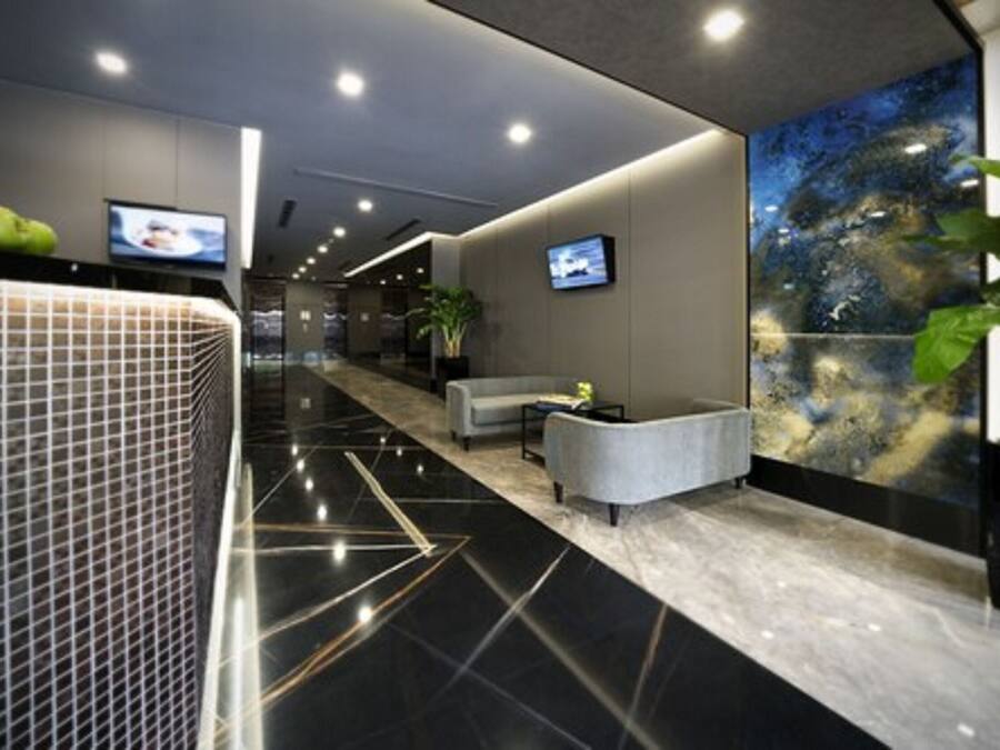 A modern hotel lobby with a black and white marble floor, a seating area with a grey sofa, and a large abstract painting on the wall.