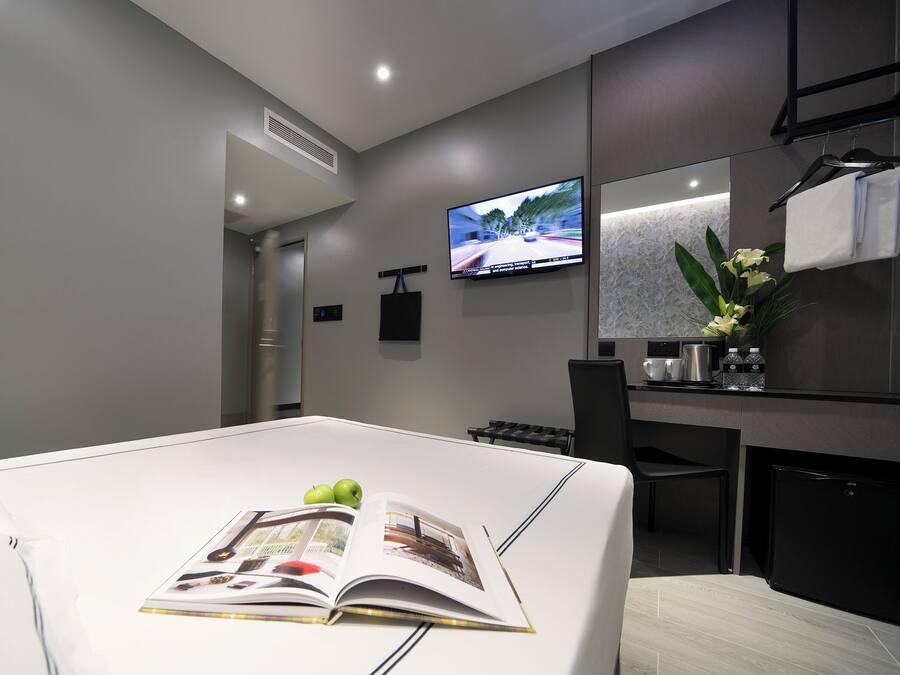 Una habitación de hotel moderna con una cama grande, un televisor de pantalla plana montado en la pared, una pequeña zona de cocina y un baño visible a través de una puerta abierta.