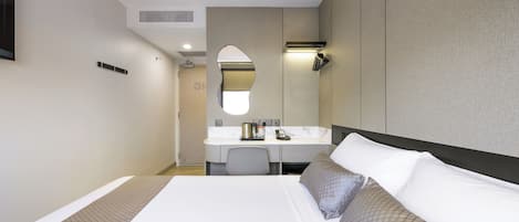 Una habitación de hotel con cama, escritorio, espejo y una pequeña kitchenette.