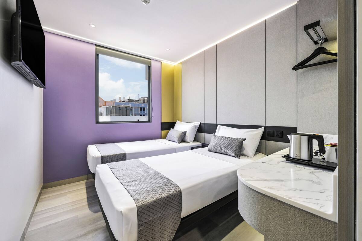 Quarto de hotel moderno com duas camas, bancada de mármore e vista para a cidade.