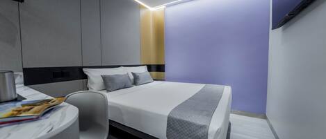 A modern hotel room with a neatly made bed, a bedside table with a magazine, and a chair.
