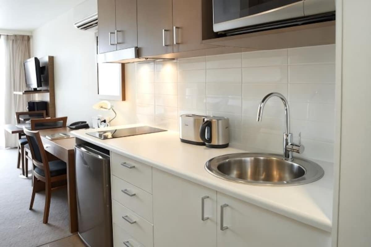 Una cocina moderna con un lavamanos de acero inoxidable, un tostador y un microondas. Hay un comedor con sillas y una mesa.