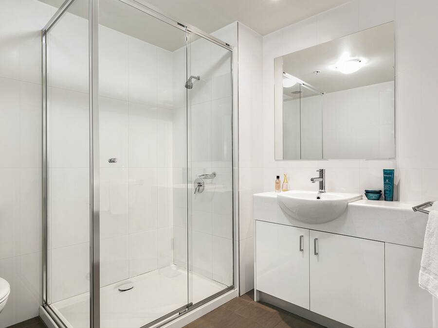 A modern bathroom with a glass-enclosed shower, a white sink, and a large mirror.