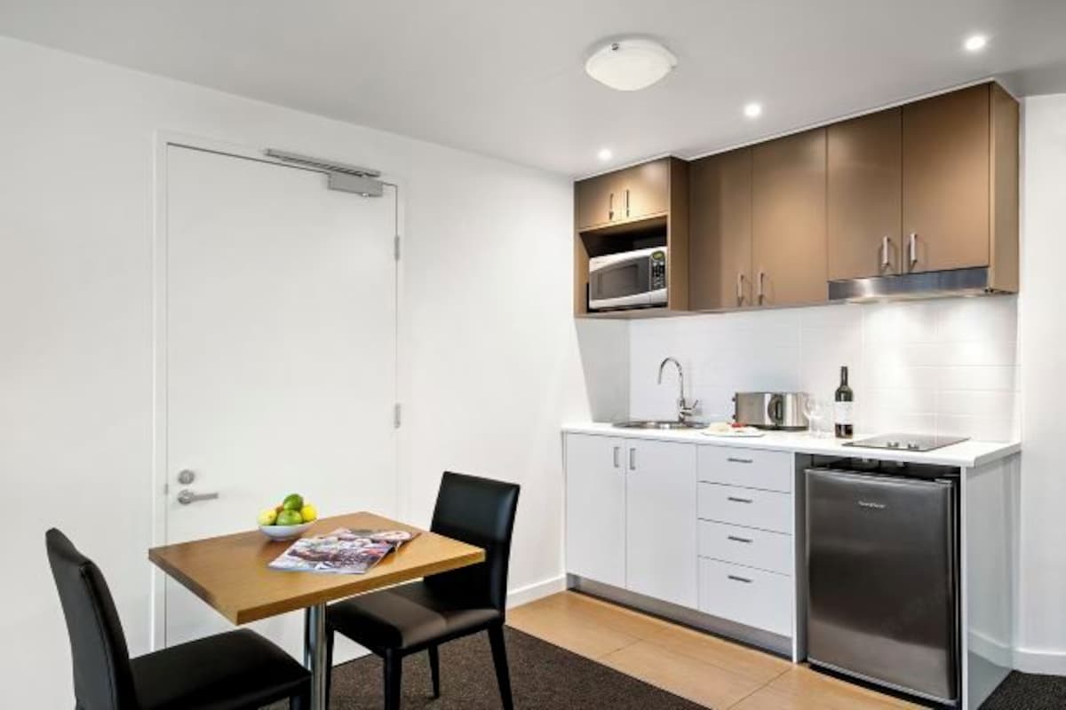 Una cocina compacta con armarios blancos, un microondas, un fregadero y un refrigerador.