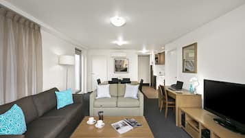 A modern hotel room with a sofa, a coffee table, a TV, a desk, and a chair.