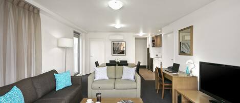 A modern hotel room with a sofa, a coffee table, a TV, a desk, and a chair.