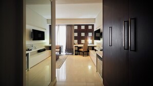 A modern hotel room with a kitchenette, a dining area, and a TV mounted on the wall.