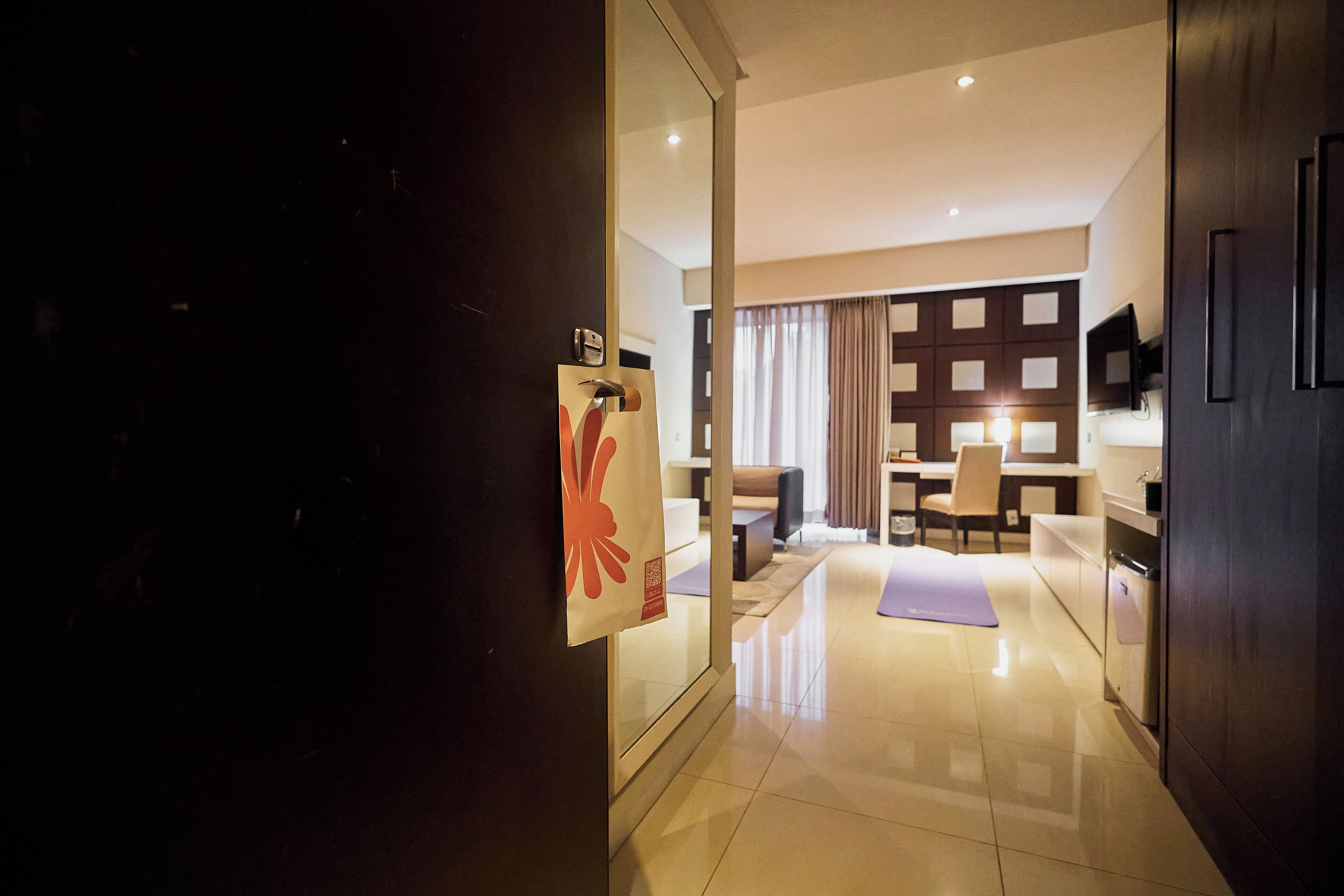 Une chambre d’hôtel moderne dotée d’un grand miroir, d’une porte en bois et offrant une vue sur l’espace de vie, avec un canapé et des rideaux.