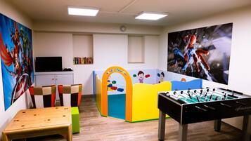 Een kamer met een tafelvoetbaltafel, een klein tafeltje, kleurrijke stoelen, een boekenkast en een televisie.