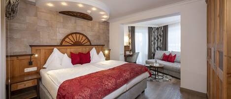 A hotel room with a large bed, a wooden headboard, a stone accent wall, a seating area with a sofa, and a small table.