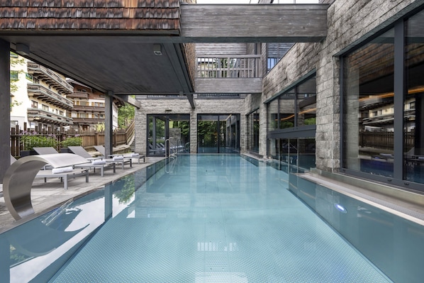 Una piscina interior moderna con agua cristalina, rodeada de paredes de piedra y amplios ventanales.