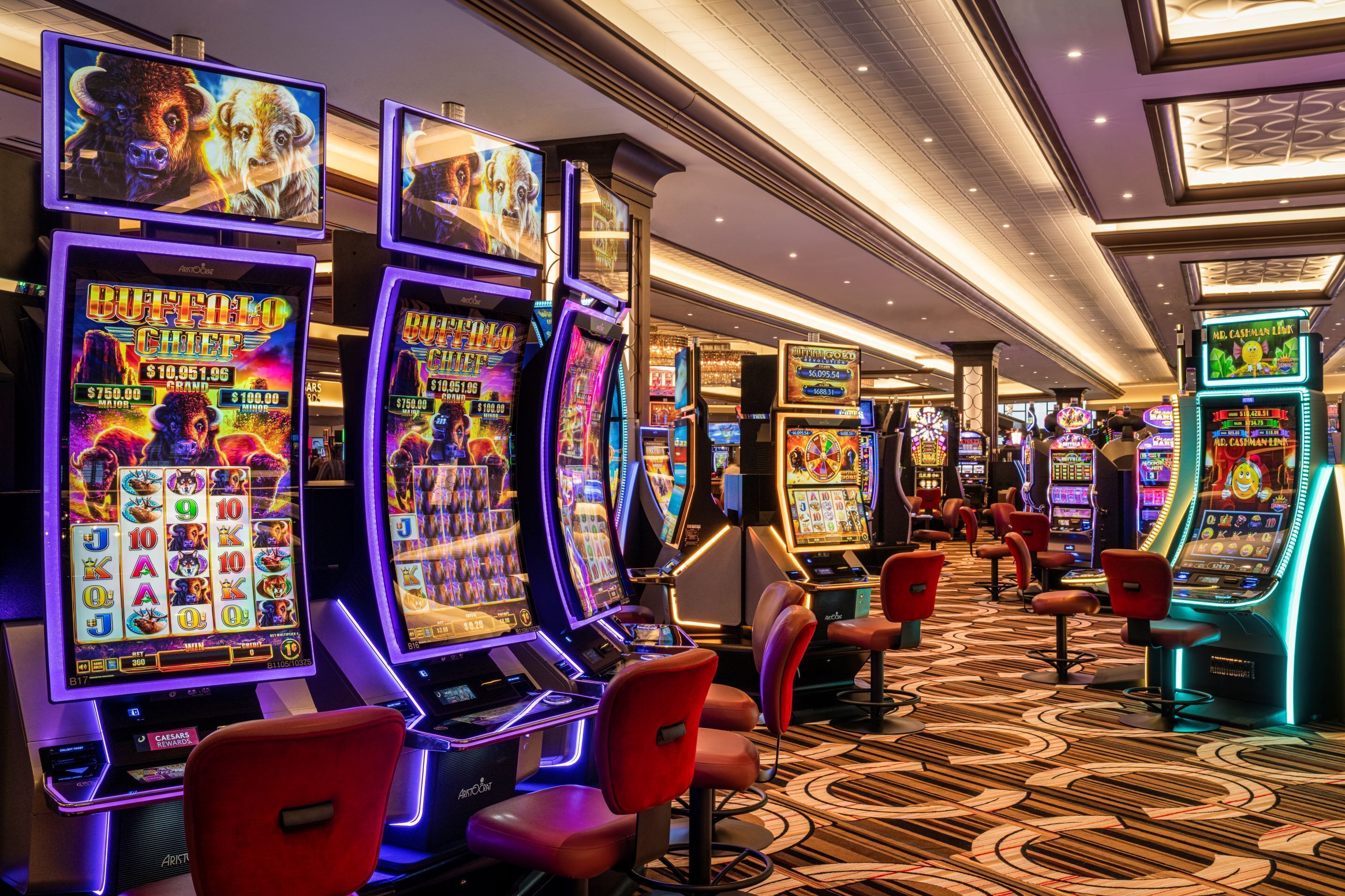 Un casino con máquinas tragamonedas, sillas rojas y una alfombra estampada.