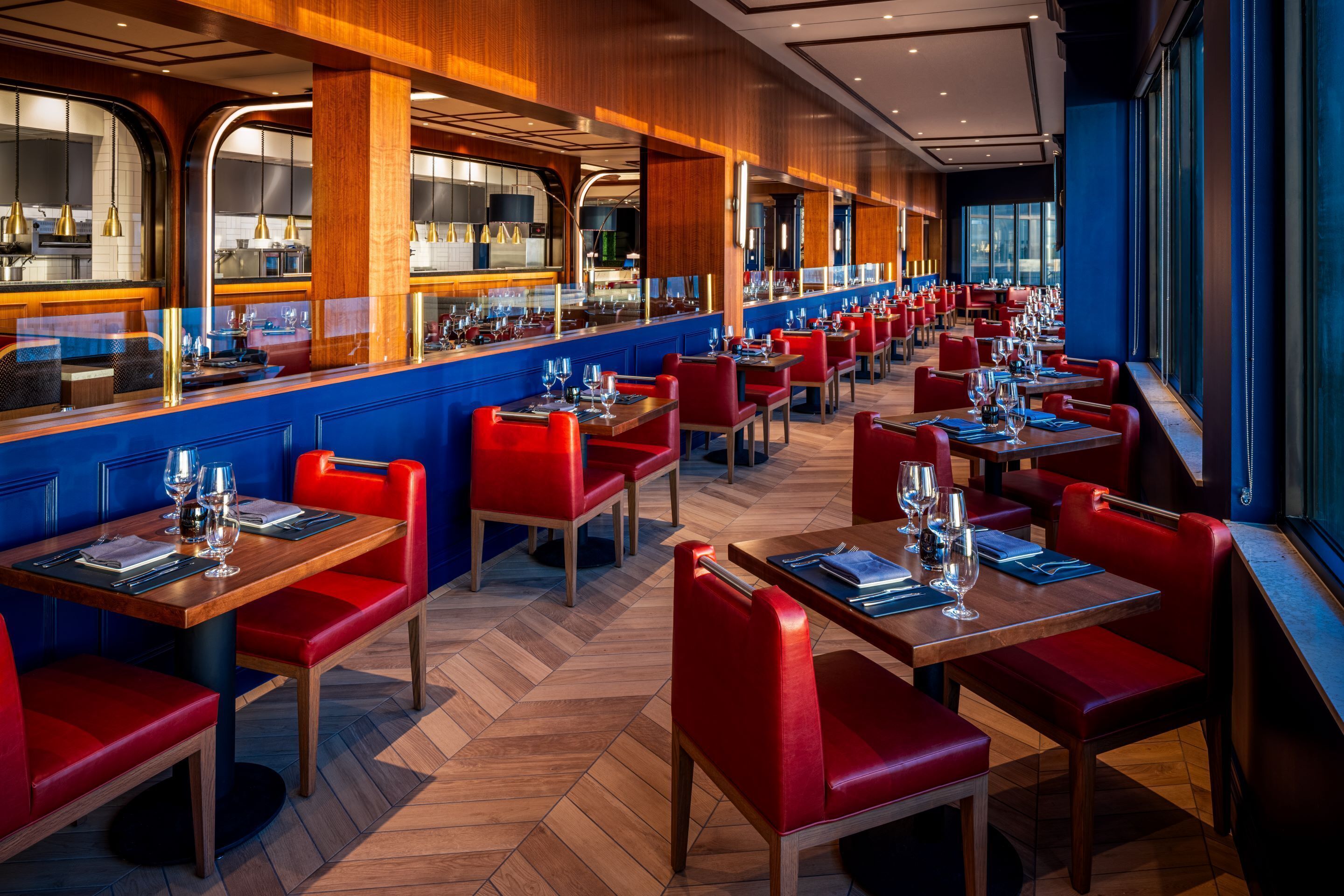 Um restaurante com um balcão comprido, cabines estofadas em vermelho e um padrão de piso em herringbone.