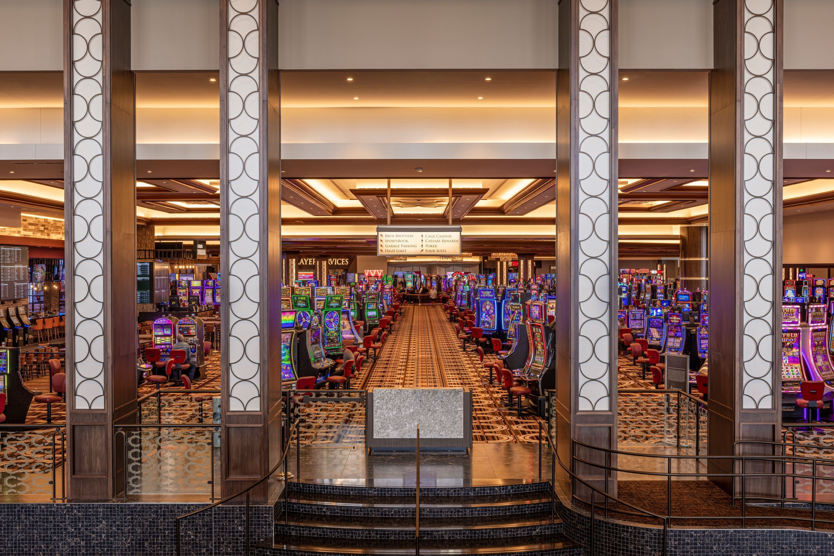 A casino floor with slot machines, a bar area, and a sign indicating services like cage cashier and sportsbook.