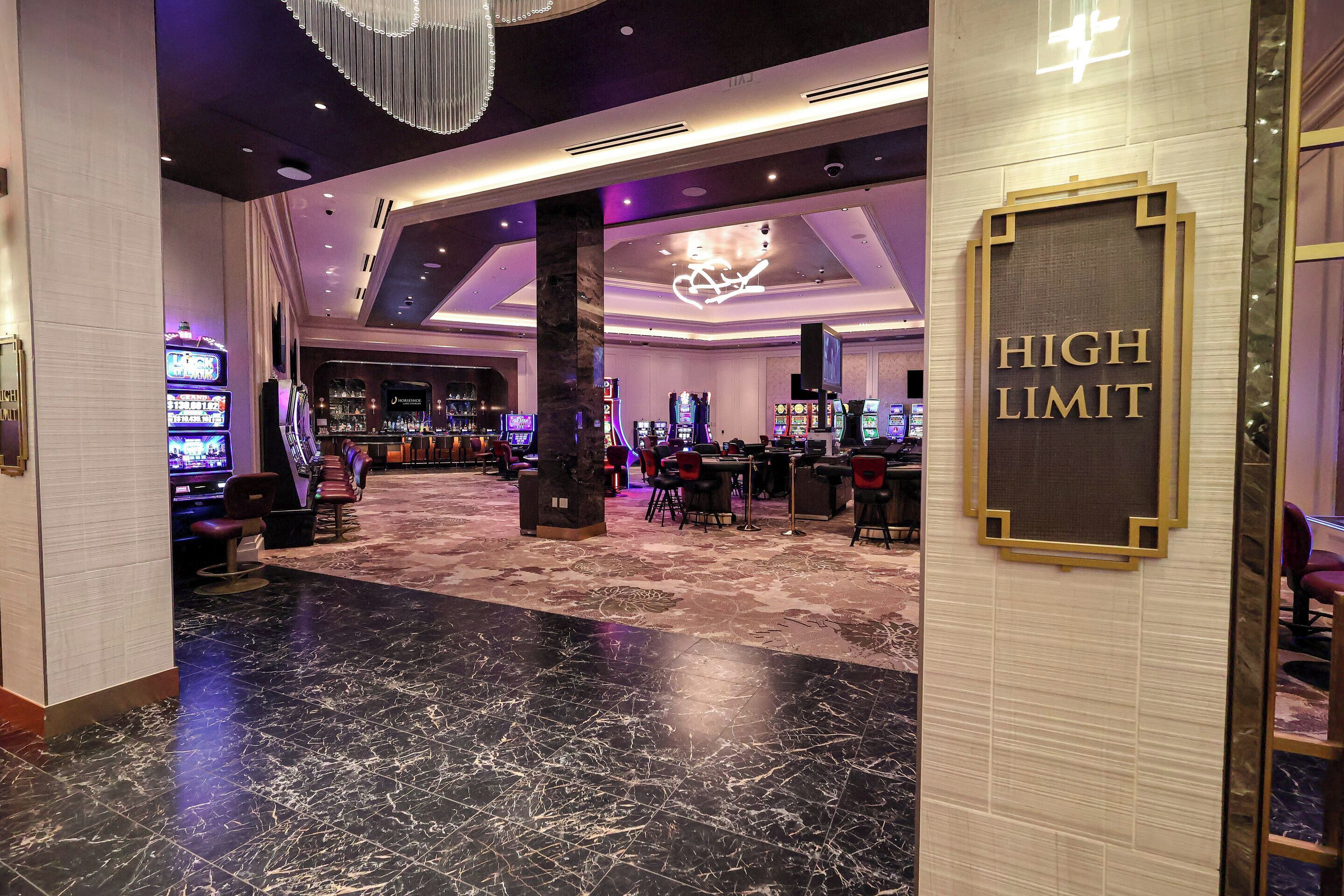 Interior de un casino con mesas de juego, sillas y un letrero que dice 'HIGH LIMIT'.