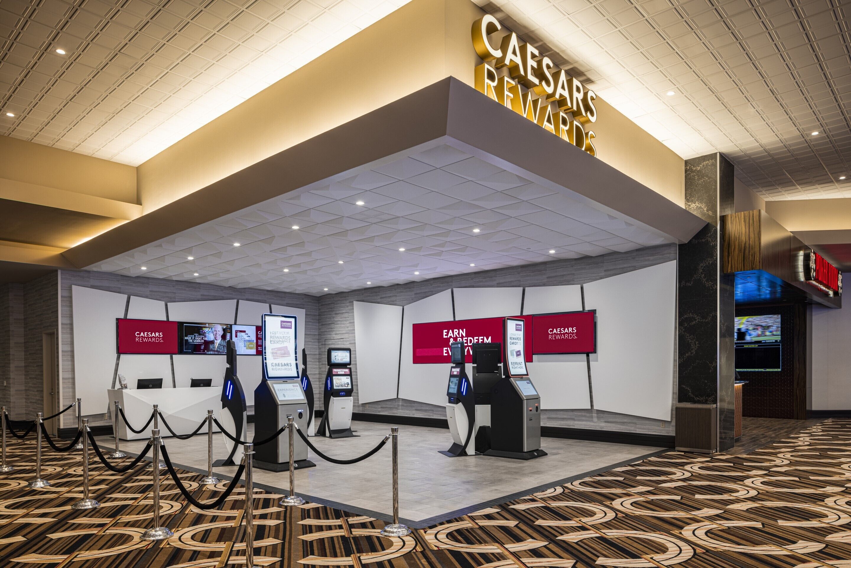 Un moderno vestíbulo de hotel con un letrero de Caesars Rewards, quioscos de autoservicio y un piso con diseño.