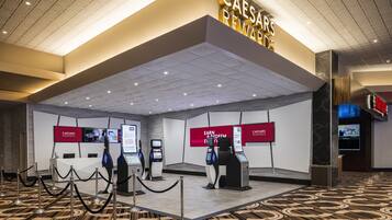 A modern hotel lobby with a Caesars Rewards sign, self-service kiosks, and a patterned floor.