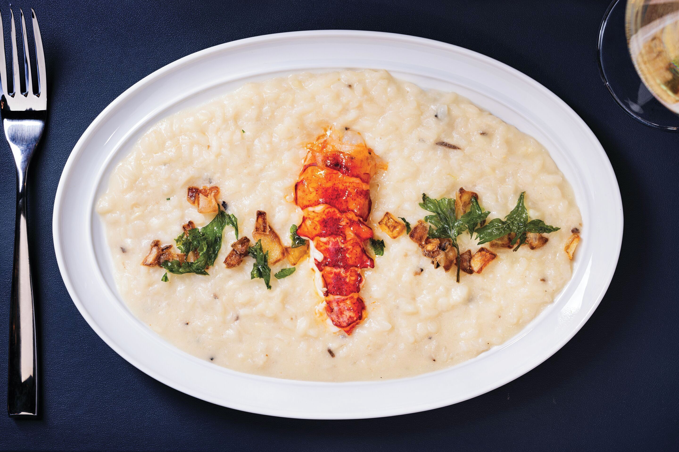 A white oval plate with a creamy dish, garnished with herbs and fried elements, on a dark surface.