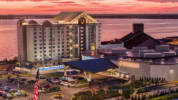 A hotel with a large building, a parking lot, and a body of water in the background. - Horseshoe Lake Charles Hotel & Casino -  A Caesars Rewards Destination (Westlake)
