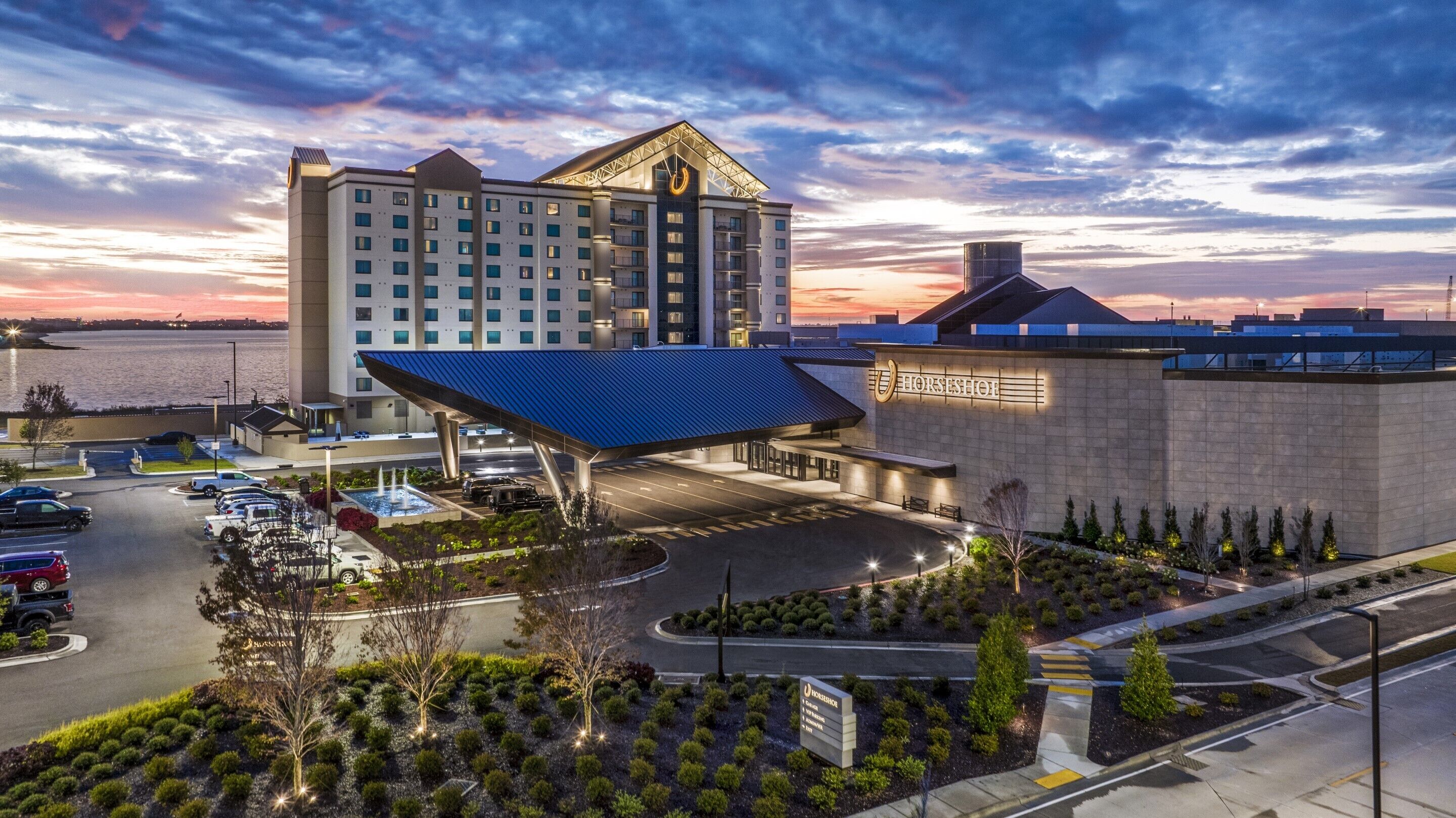 A hotel with a large parking lot, a covered entrance, and a view of the water.