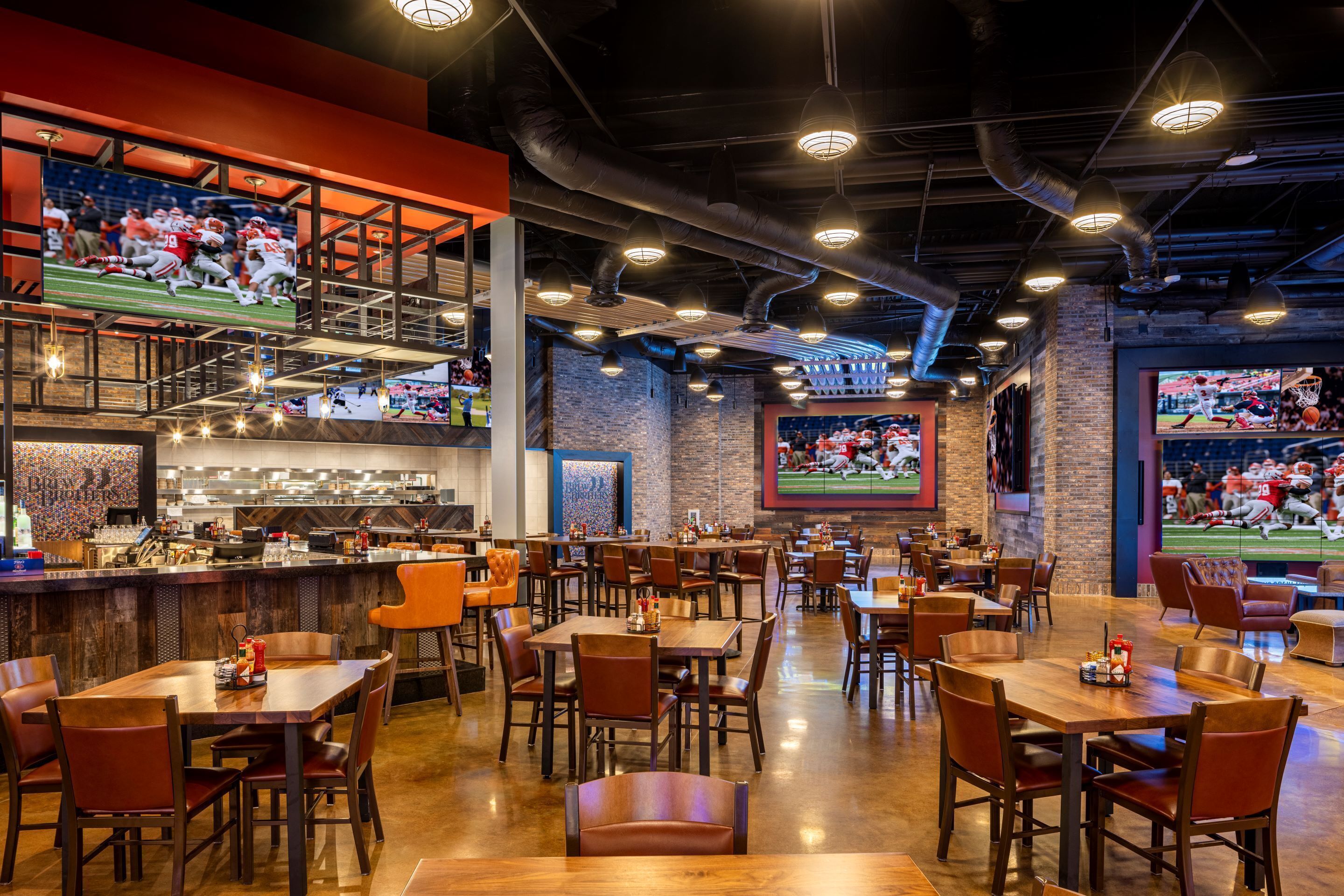 Un restaurant doté de nombreuses tables et chaises, d’un bar et d’écrans diffusant des événements sportifs.