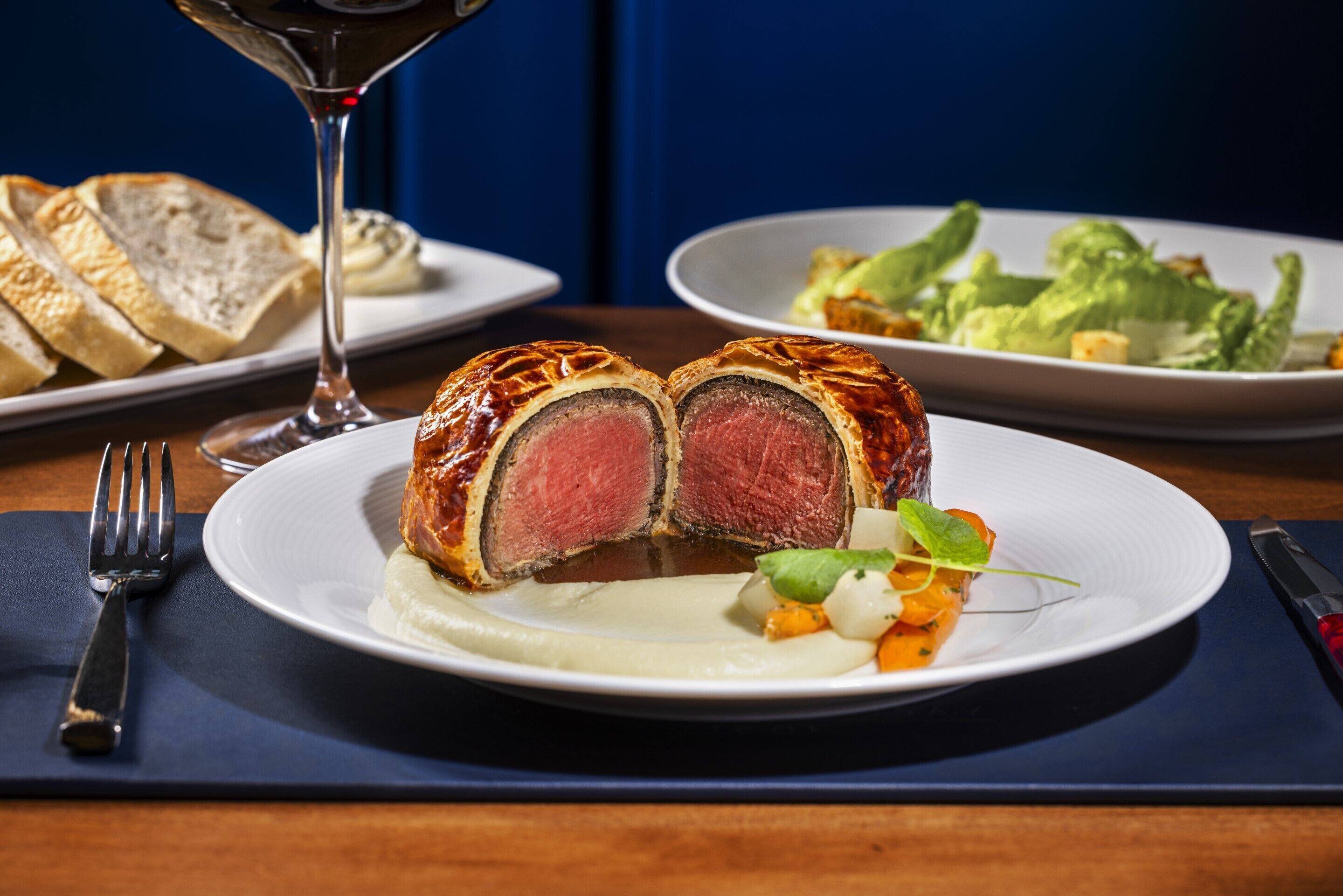 A plate of sliced beef with a side of vegetables and a glass of red wine on a table.