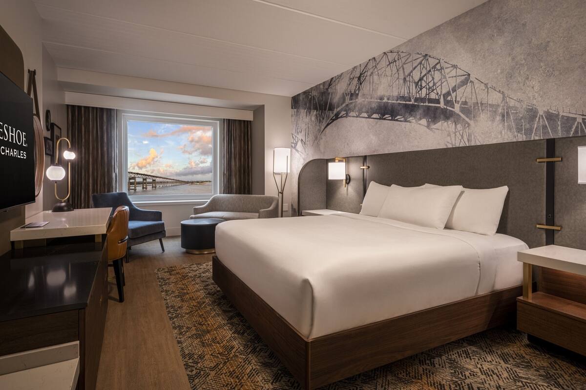 A hotel room with a large bed, a desk with a chair, a TV, and a window with a view of a bridge.