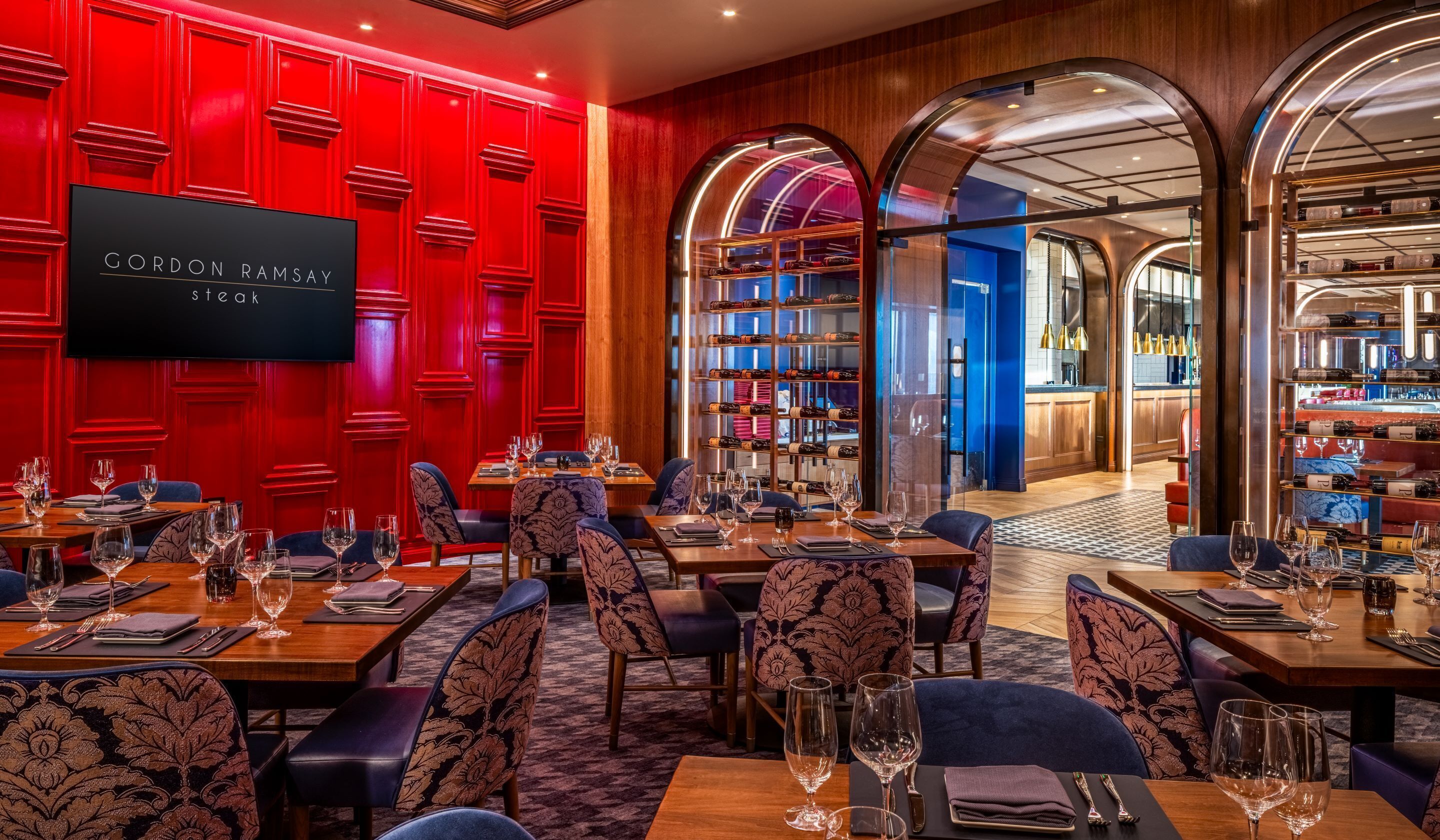 A restaurant with red paneled walls, a wine cellar, and a bar area.