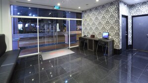 A modern lobby with a reception desk, a large glass door entrance, and patterned wallpaper. - Value Hotel Nice (Singapore)