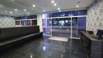 Un vestíbulo moderno con un mostrador de recepción, una zona de espera con un banco y una puerta de cristal que da al exterior.
