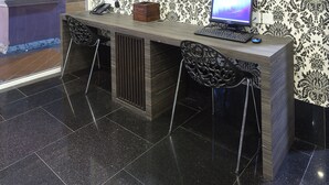 A reception desk with a computer, two chairs, and a patterned wallpaper. - Value Hotel Nice (Singapore)