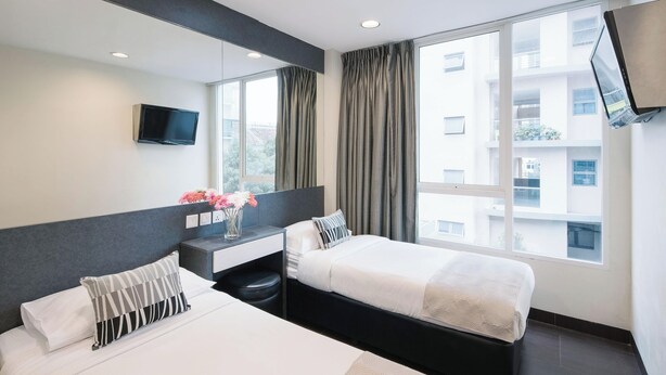 A modern hotel room with a large bed, a bedside table, a TV mounted on the wall, and a window with curtains. - Value Hotel Nice (Singapore)