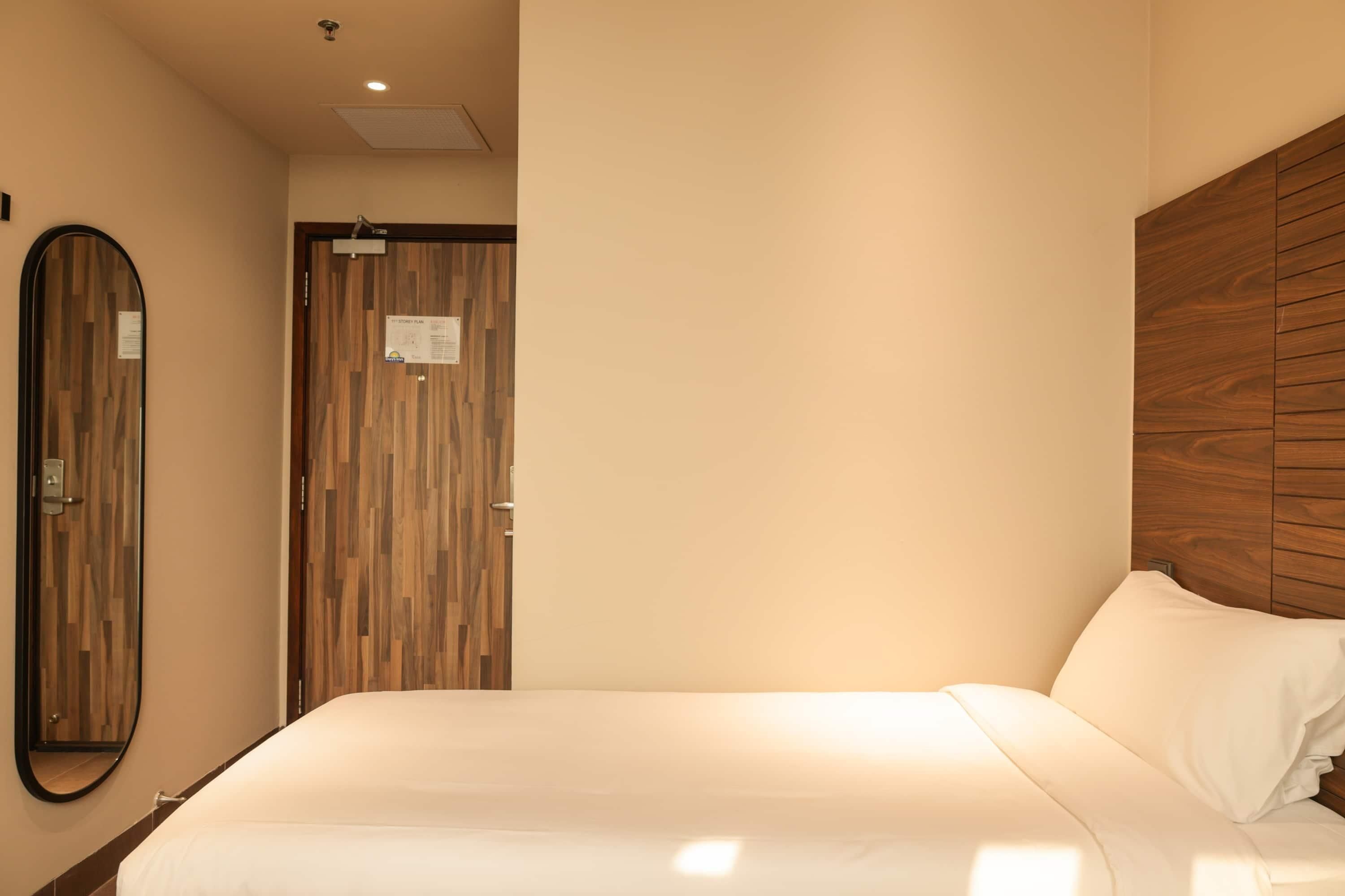 A hotel room with a bed, a wooden headboard, a mirror, and a door with a vertical wood panel design.