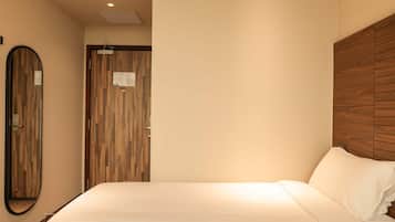 A hotel room with a bed, a wooden headboard, a mirror, and a door with a vertical wood panel design.