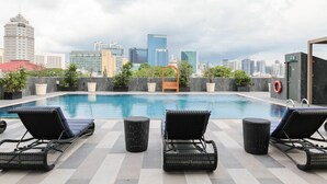 Una piscina en la azotea con sillones de descanso, un flotador salvavidas y un horizonte urbano al fondo.