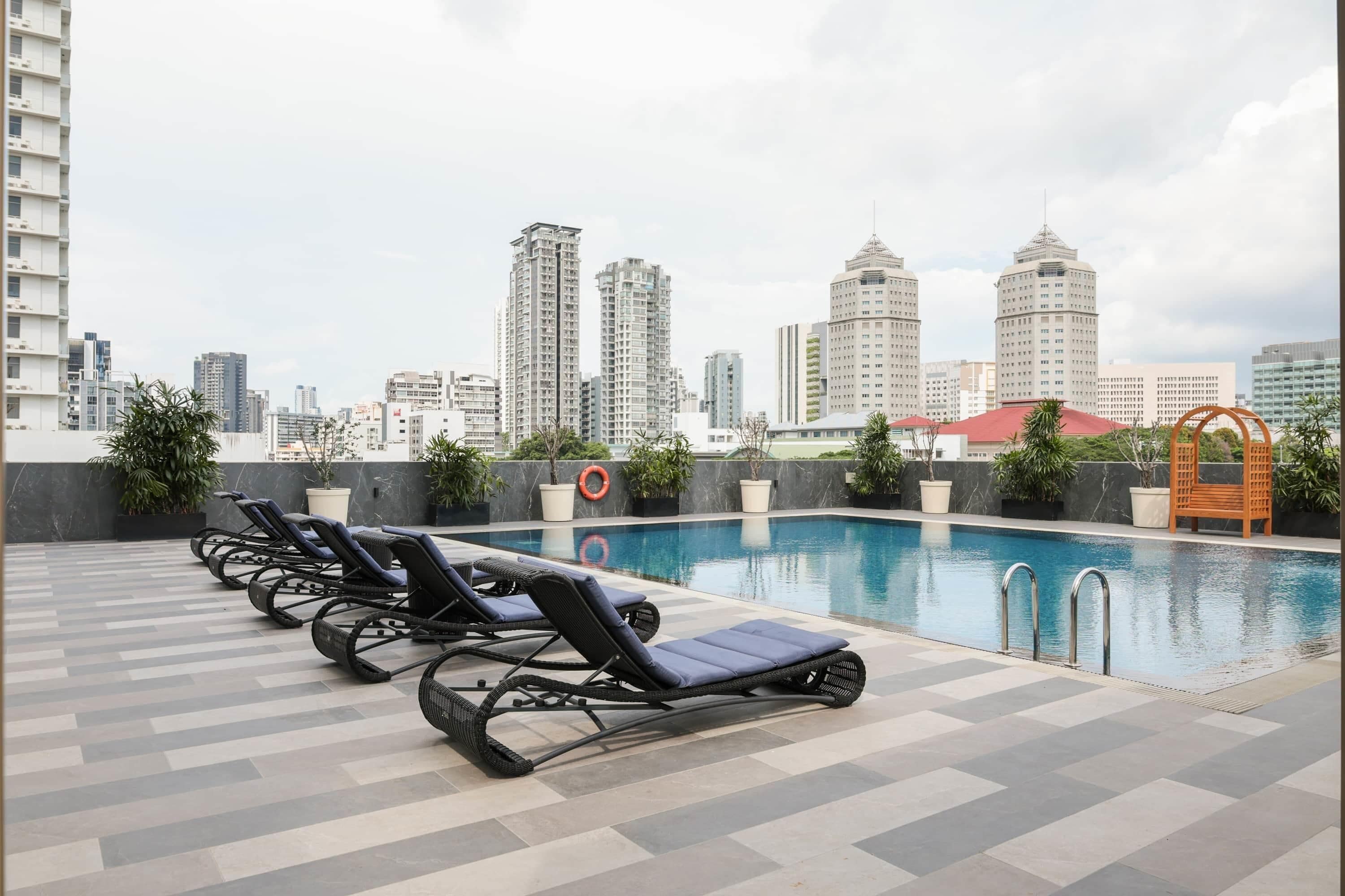 A rooftop pool with lounge chairs, a city skyline in the background, and a view of tall buildings.
