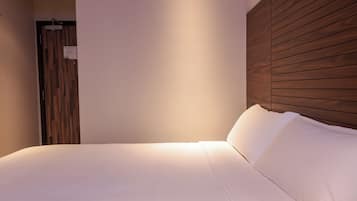 A neatly made bed with white linens, a wooden headboard, and a wall-mounted light fixture.