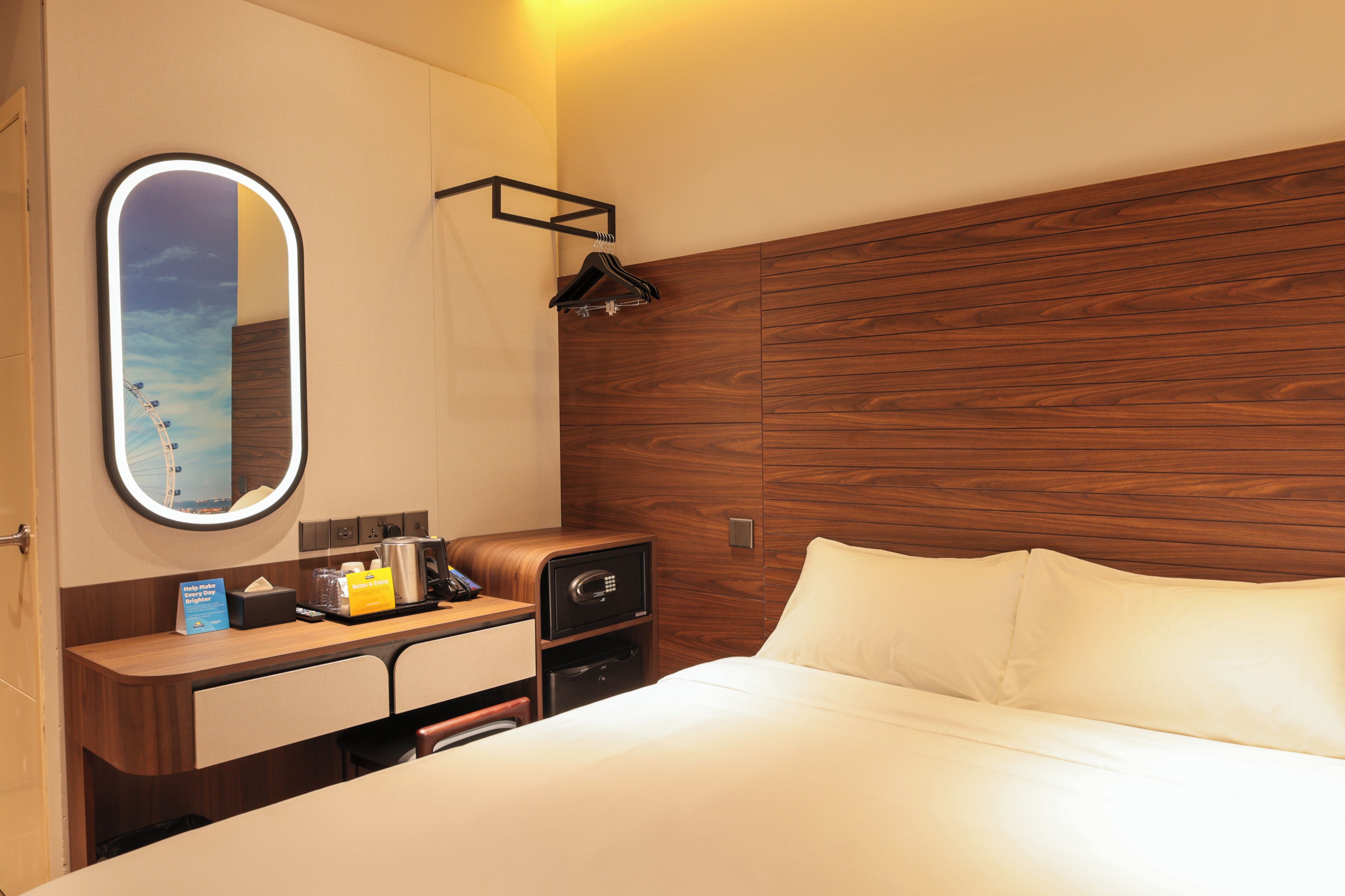 A hotel room with a wooden headboard, a bedside table with a lamp, a mirror, and a bed with white linens.