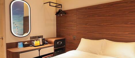 Habitación de hotel con cabecera de madera, una mesita de noche con lámpara, un espejo y una cama con ropa blanca.