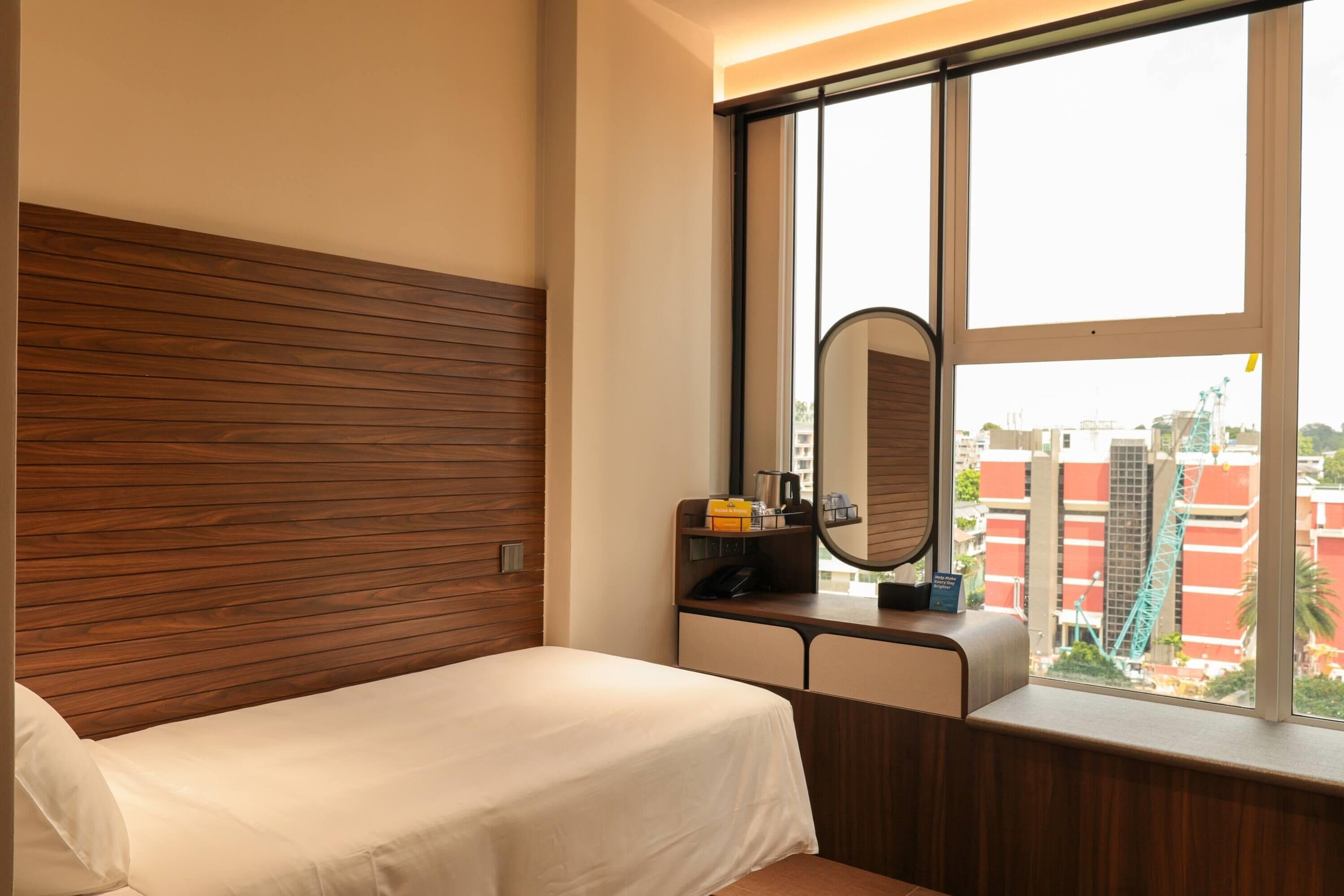 Habitación de hotel con cabecera de madera, cama, escritorio con espejo y ventana con vista a la ciudad.